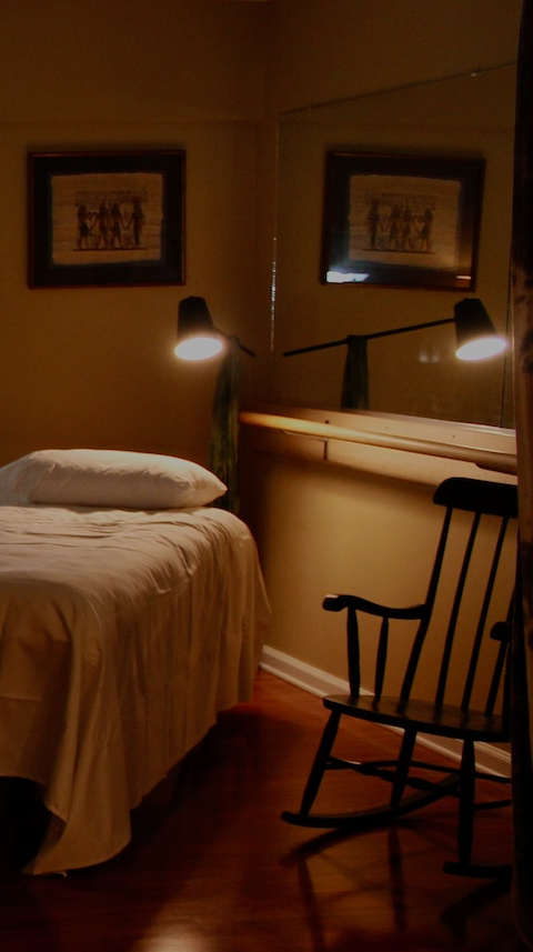 Picture of the Lower Bucks Acupuncture clinic. One acupuncture bed with lamplight shining on it, next to a rocking chair.